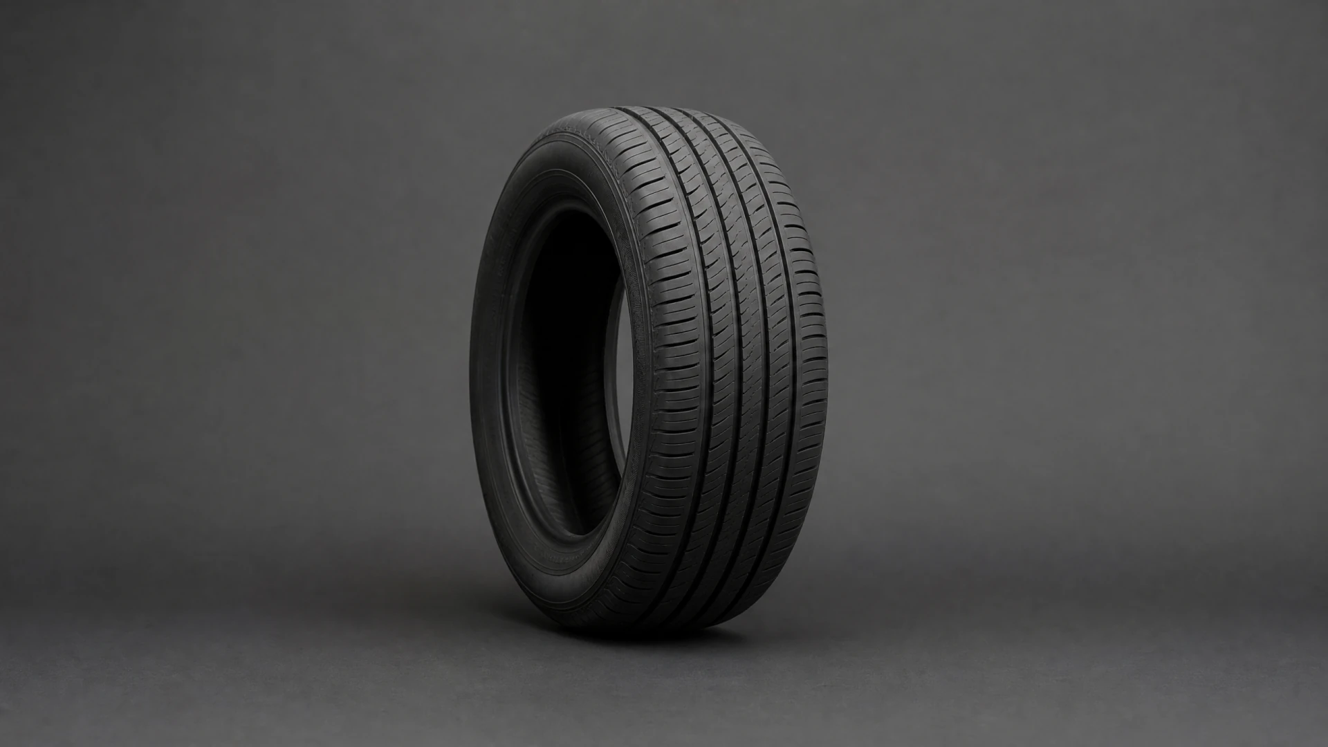 A black car tire with a ribbed tread pattern stands upright at an angle against a dark gray background.