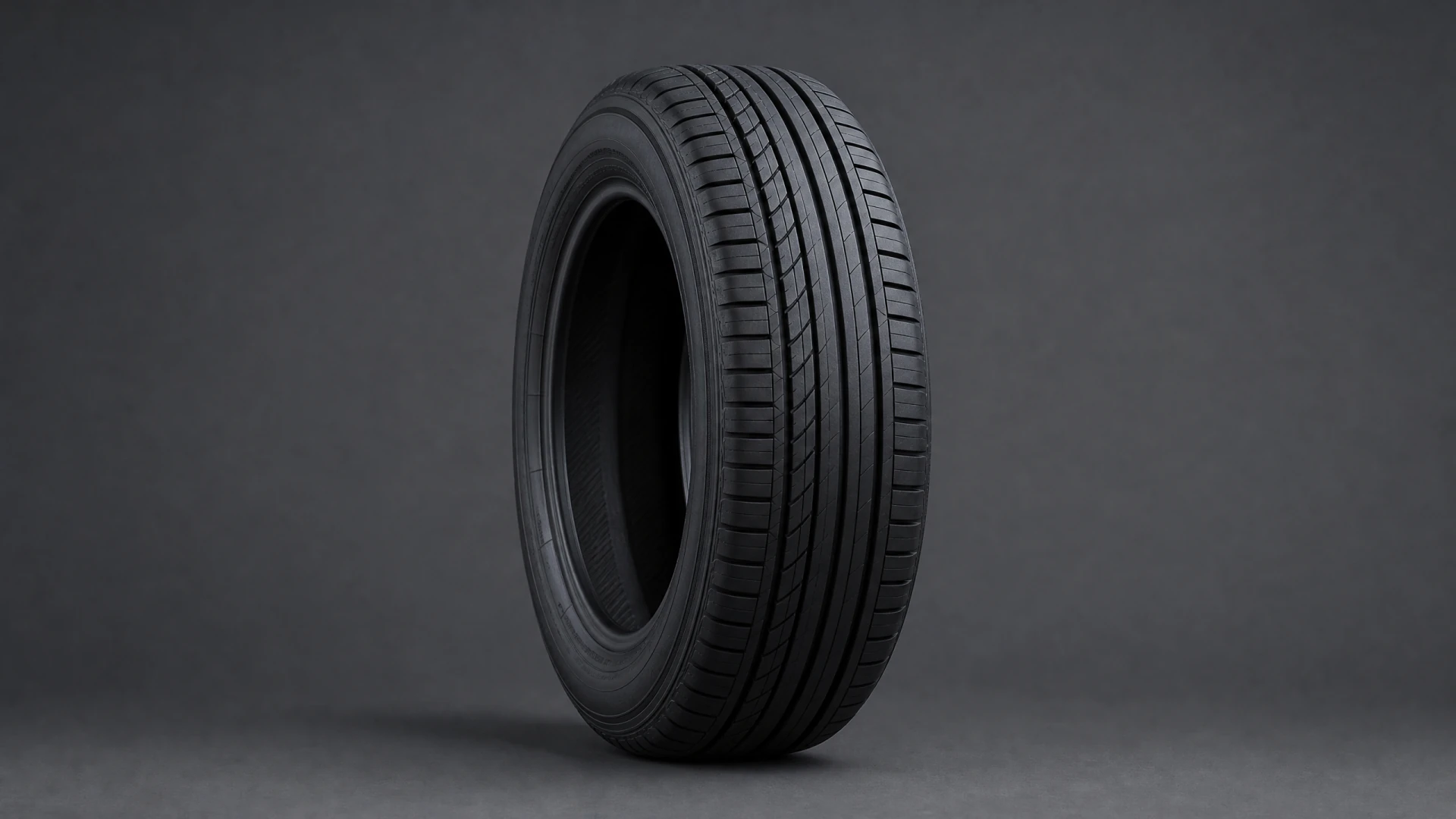 A black car tire with a multi-groove tread pattern, photographed upright against a dark gray studio background.