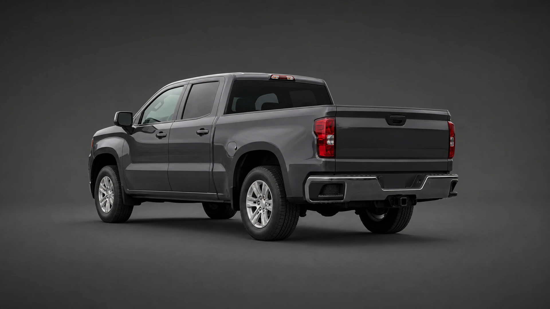 A dark gray crew-cab pickup truck shown from the rear three-quarter angle in a studio setting, displaying its bed, chrome bumper, and alloy wheels.
