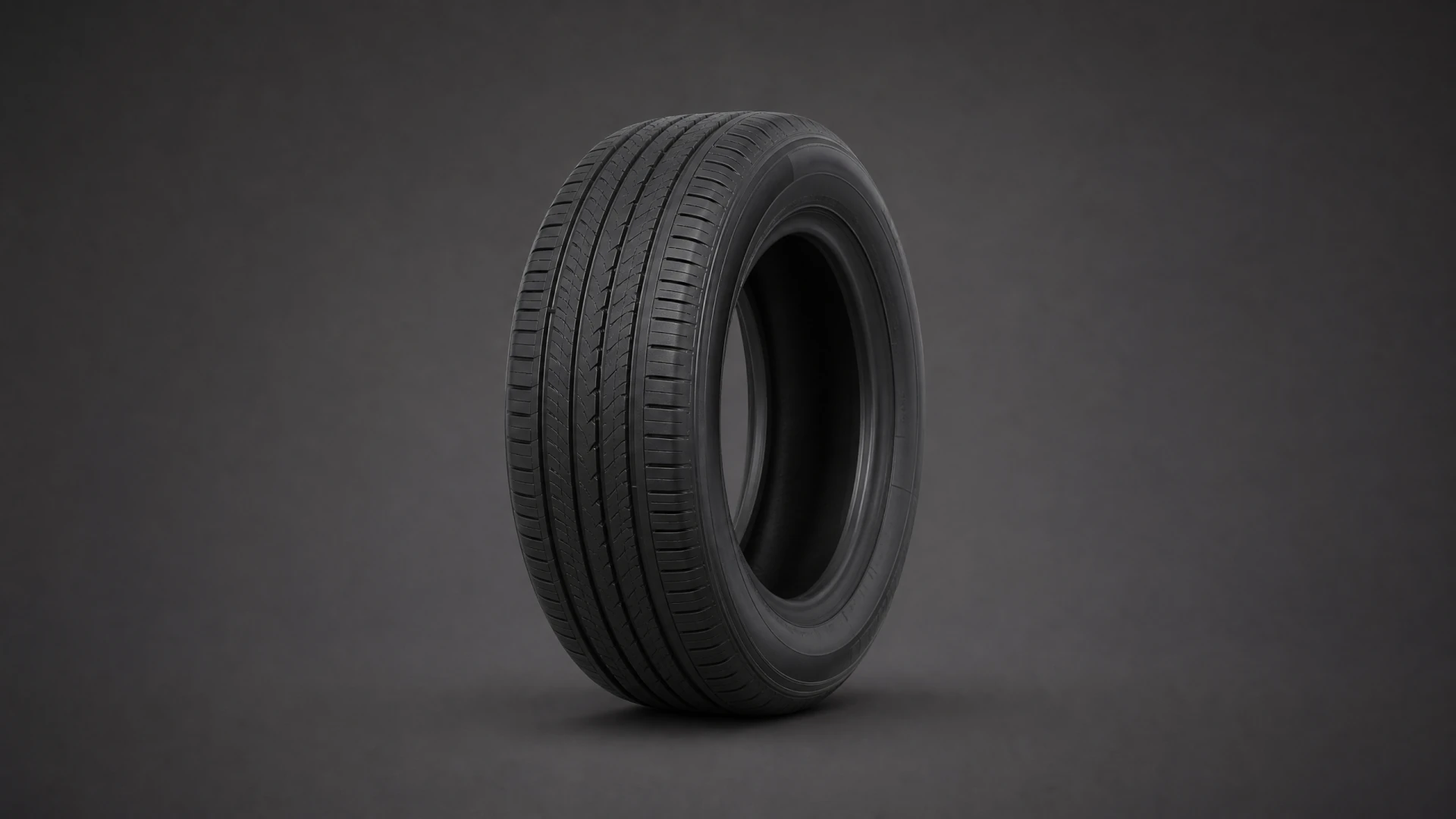 A black car tire with a multi-groove tread pattern stands upright against a dark gray studio background.