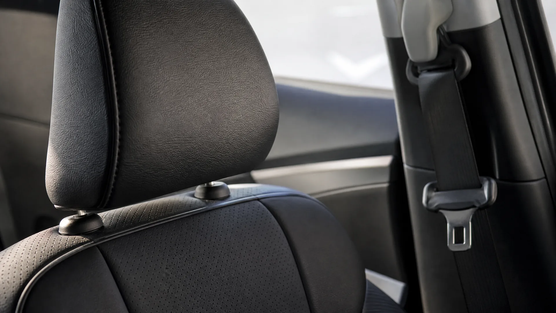 Close-up of a black perforated leather car seat with headrest, with a seat belt and buckle on the pillar behind it.