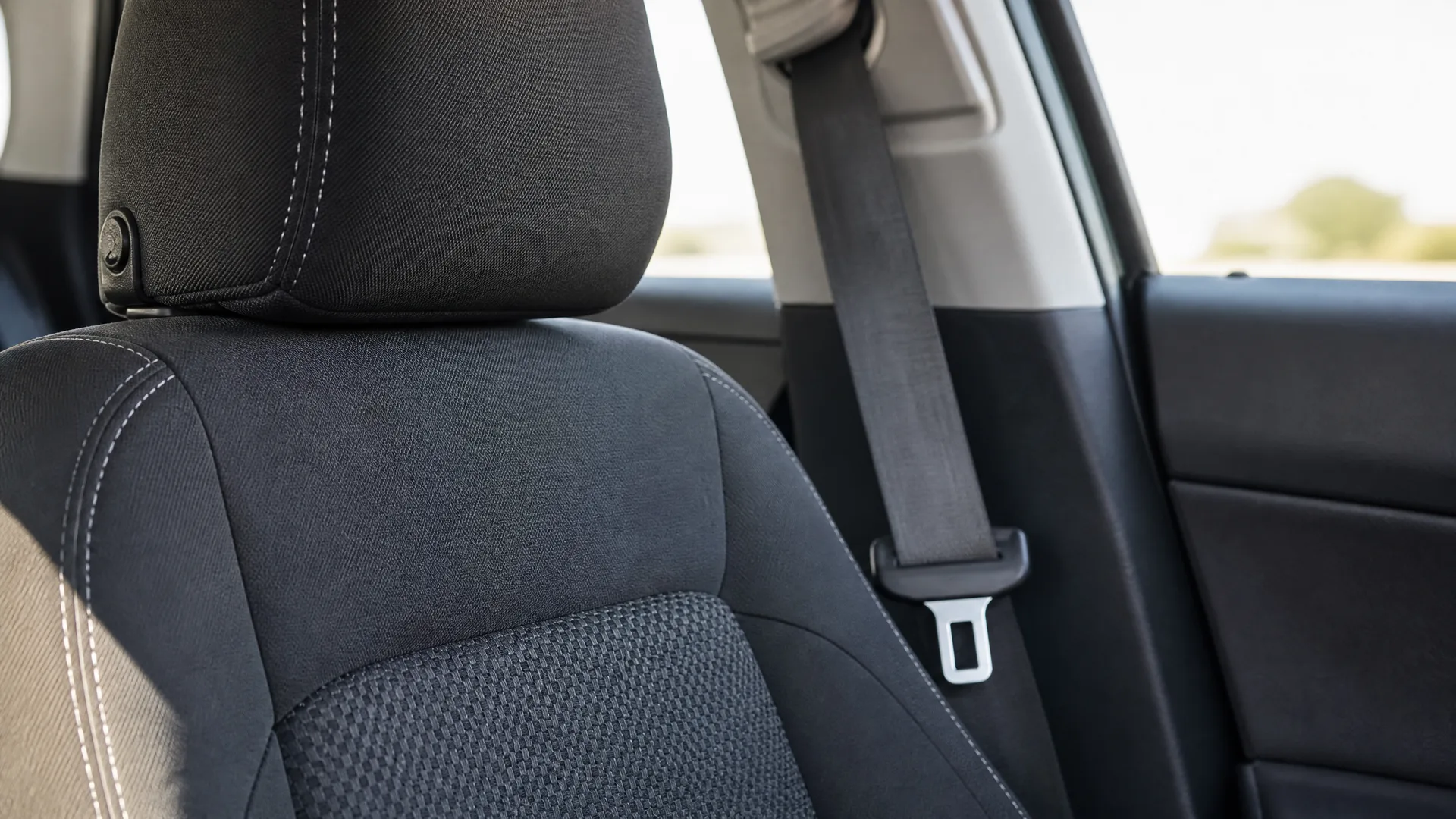 Close-up of a black cloth car seat with headrest and a seat belt with metal buckle beside the rear door window.
