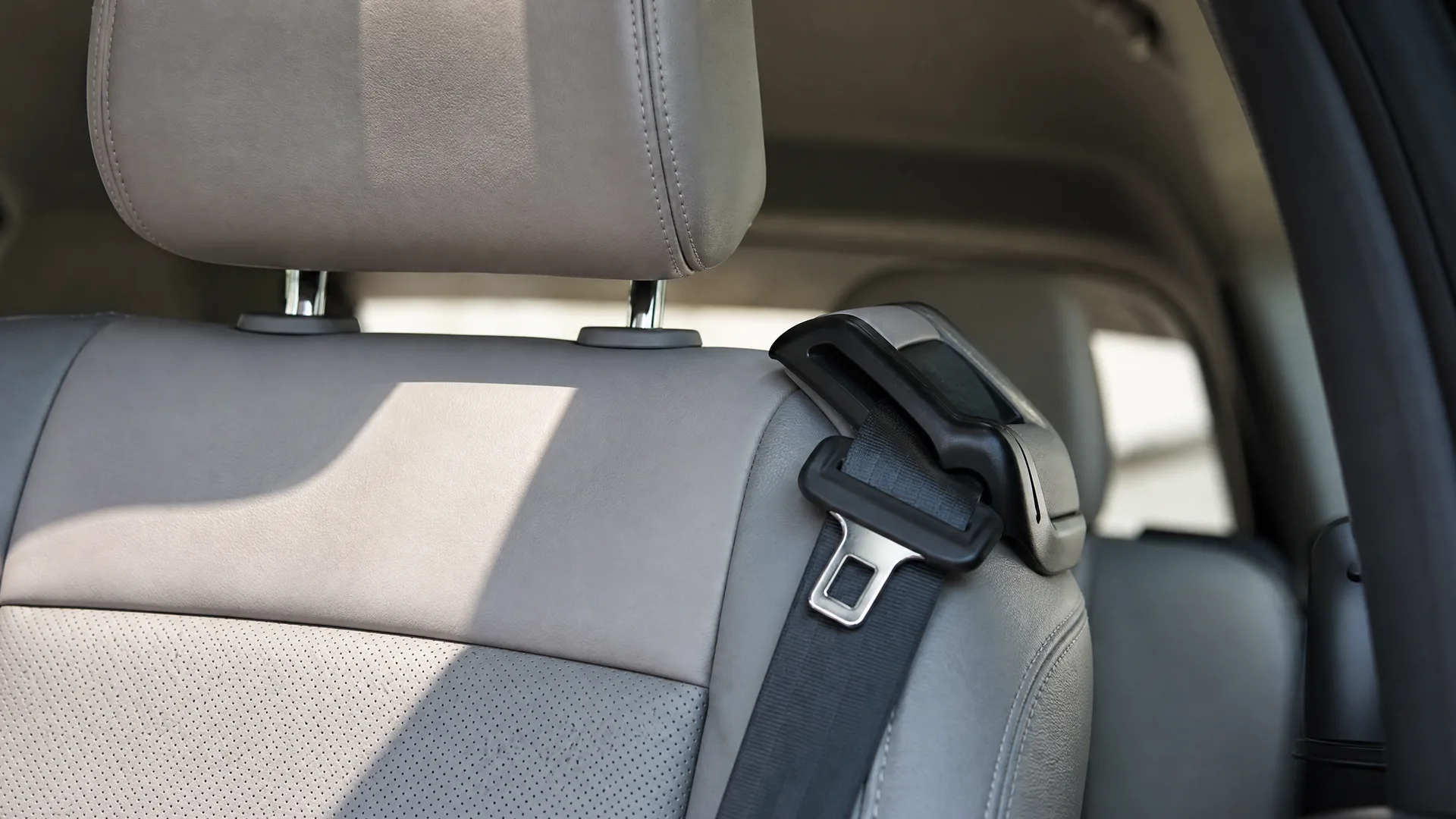 Close-up of a gray car seat with headrest and a black seat belt buckle latched into its receiver inside a vehicle.