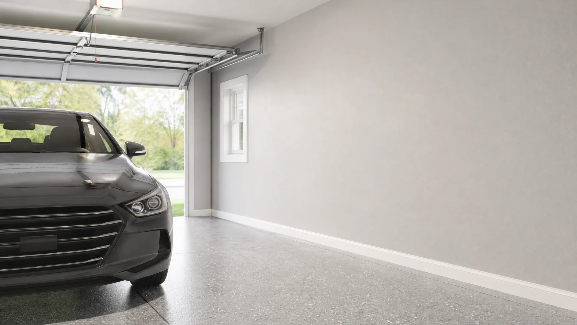 Interior of an empty garage with a speckled epoxy floor, gray walls, a small window, and an open sectional door with the front half of a dark gray sedan parked inside.
