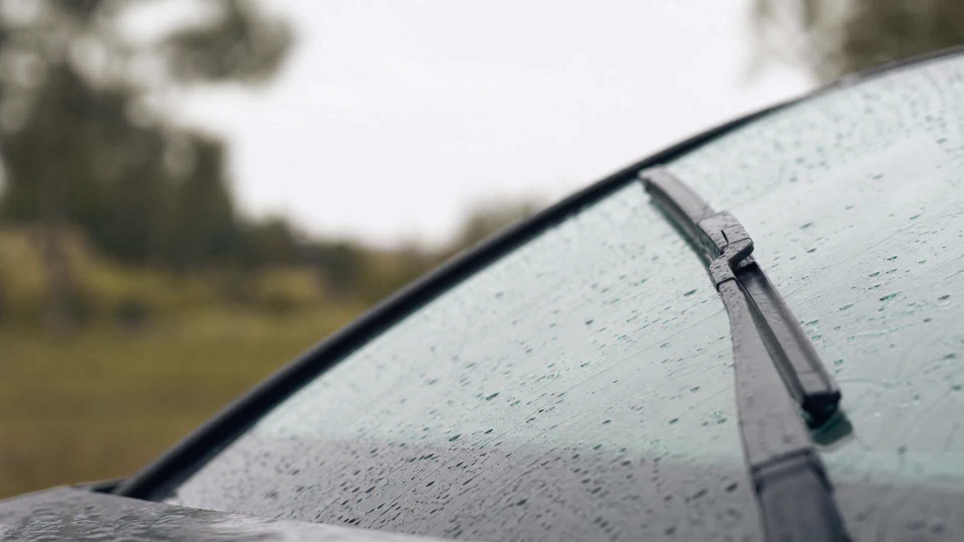 A rain-covered car windshield with a windshield wiper blade resting on the wet glass.