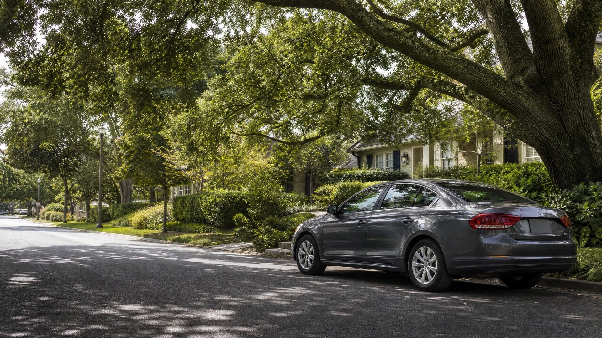 A gray sedan parked along a shaded residential street lined with large trees and houses.