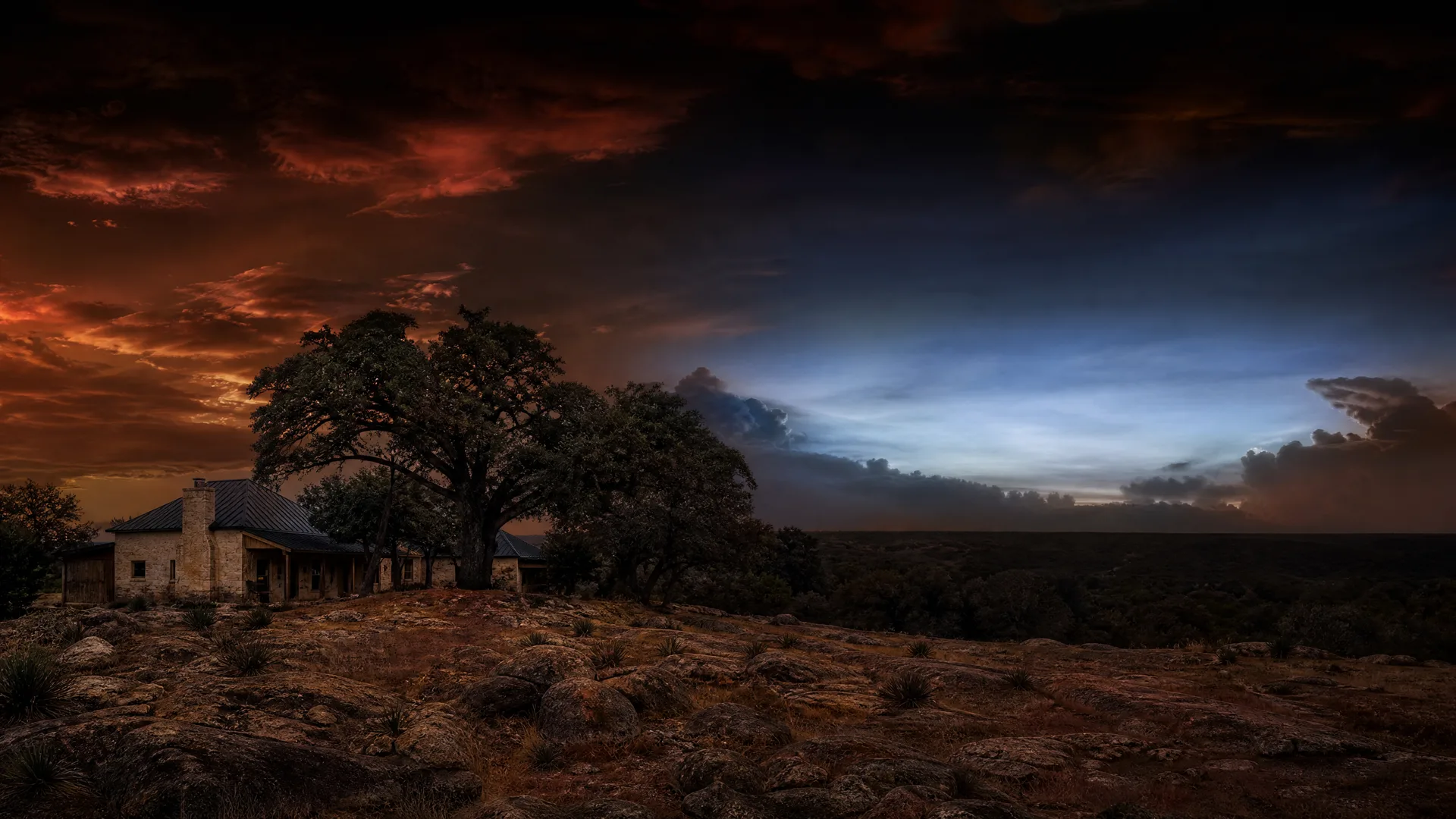 A stone house with a metal roof stands beneath large oak trees on a rocky hilltop at dusk, under a sky with orange and dark blue clouds.